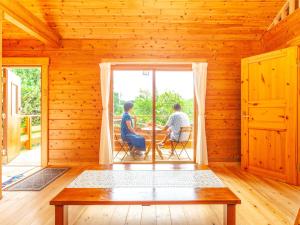 zwei Männer sitzen an einem Tisch in einem Holzhaus in der Unterkunft 石垣島コテージAkeeesi365 in Ishigaki-jima