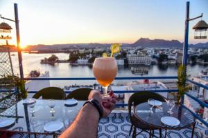 a person holding a drink at a table on a balcony at Hotel Casa by the lake in Udaipur