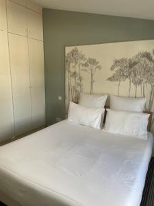 a white bed with white pillows and a painting on the wall at Hôtel Le Martray in Ars-en-Ré