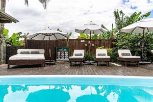 una piscina con 2 sillas y sombrillas junto a en Lindo condomínio em meio à natureza em Bombinhas VLE, en Bombinhas
