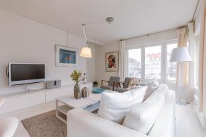 a white living room with a white couch and a tv at Pleasant Apartment for Families close to the beach in De Haan