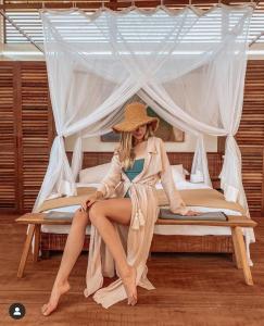 a woman in a hat sitting on a bed at Limbo Atins Chalets - Lençóis Maranhenses in Atins