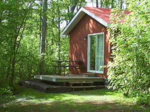 a small red cabin with a porch in the woods at New Glasgow Highlands Campground cabins in New Glasgow +13 photos