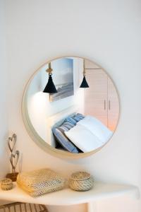 a round mirror on a white wall above a bed at Sagma calm apartment with amazing sea view in Perissa