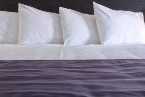 a bed with white pillows and purple sheets at Stonecroft Inn in Windsor