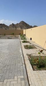 a brick sidewalk next to a building with mountains in the background at Al Ghadeer Maison Masfout in Sharīyah