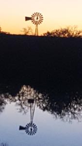 een weerspiegeling van een windmolen in het water voor een zonsondergang bij The White House at SF Ranch in Comanche