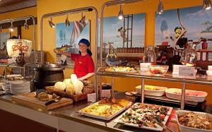 une femme debout derrière une ligne de buffet avec de la nourriture dans l'établissement LEGOLAND Pirates´ Inn Motel, à Billund