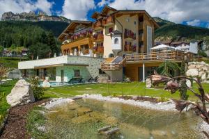 a house with a pond in front of it at Nature Wellness Hotel Renato in Vigo di Fassa