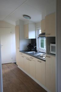 a kitchen with white cabinets and a sink and a microwave at Vakantiepark Dennenoord in Den Burg