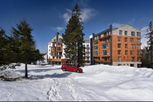 een rode auto geparkeerd in de sneeuw voor een gebouw bij APLEND Hotel Ovruč in Štrbské Pleso