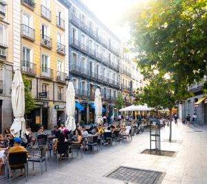 uma rua da cidade com pessoas sentadas em mesas e guarda-chuvas em Hostal Persal em Madrid