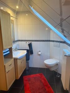 a bathroom with a sink and a toilet and a red rug at Ferienwohnung Brügge - zwischen Eider & Nord-Ostsee-Kanal in Breiholz