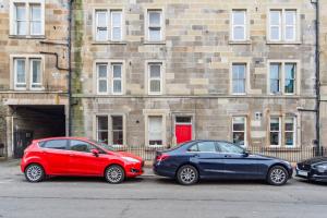 dois carros estacionados num parque de estacionamento em frente a um edifício em The Plywood Flat, Modern Style In A Traditional Tenement em Edimburgo