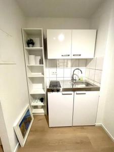 una pequeña cocina con armarios blancos y fregadero en Schickes Apartment mit Balkon in Düsseldorf, en Düsseldorf