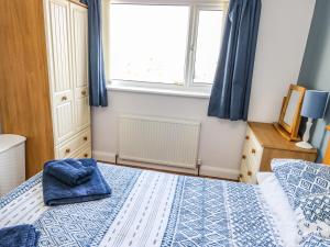 a bedroom with a bed with a blue blanket and a window at Crud Yr Awel in Amlwch