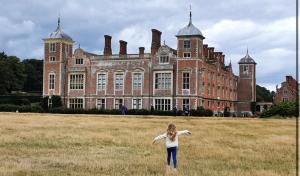 a girl standing in a field in front of a large building at Maple Hut Four Acre Farm in Aylsham
