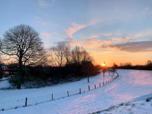 un campo cubierto de nieve con una valla y la puesta de sol en Atelier Onder de Notenboom, en Appeltern