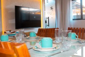 Una mesa con platos y tazas y un televisor. en Casa Riacho, en São Miguel dos Milagres