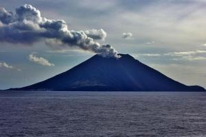 un volcán con humo saliendo de él en el océano en Via Marina, en Stromboli