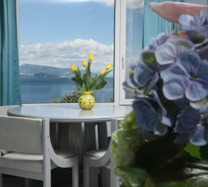 einen Tisch mit einer Vase aus Blumen und einem Fenster in der Unterkunft kon&kona hrakleitsa in Nea Iraklitsa
