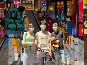 Tre persone con maschere facciali davanti a un murale di mydeer backpacker a Tainan