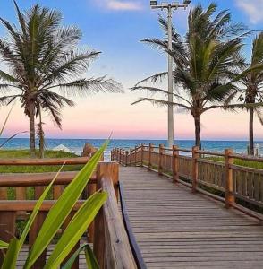 a wooden boardwalk leading to the beach with palm trees at Suítes Privativas em Guriri in Guriri +33 photos