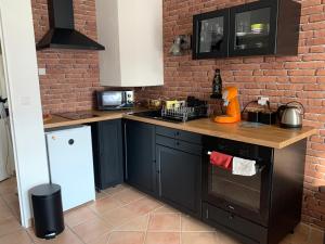 a kitchen with black cabinets and a brick wall at Cottage Duplex golf de Limère prox Orléans in Ardon