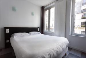 a white bed in a room with two windows at Hotel Mimosa Paris in Paris