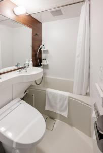 a white bathroom with a toilet and a sink at Smile Hotel Okayama in Okayama