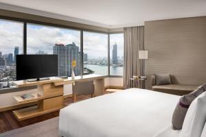 a hotel room with a bed and a desk with a television at Avani Plus Riverside Bangkok Hotel -SHA Plus Certified in Bangkok