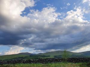 a cloudy sky with a stone wall in a field at Lavender Cottage with Parking and Beautiful Views in Carsphairn