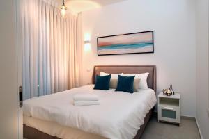 a bedroom with a bed with white sheets and blue pillows at Hi-Yam SeaView Apartments & Suites - Building Shelter Available in Bat Yam