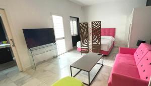 uma sala de estar com um sofá rosa e uma televisão em Ritual Alameda Suites em Sevilha
