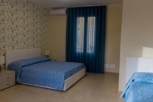 a bedroom with two beds and a window with blue curtains at Oikos - Ragusa Ibla in Ragusa