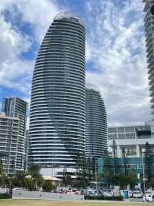 黄金海岸4 Bedroom Huge Sub Penthouse Oracle Level 31 Magnif VIEWS 260m2 Family Skyhome Sleeps 8 Adults and 2 Children, Sofa Bed Portacot, High Chair Central to Everything Resort Skyhome 5 STAR Luxury的一座高楼，前面停着汽车