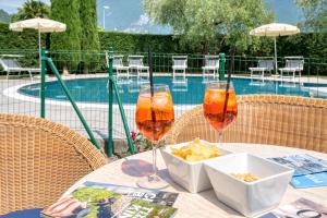 two glasses of wine and a bowl of chips on a table near a pool at Hotel Garni Al Frantoio in Arco