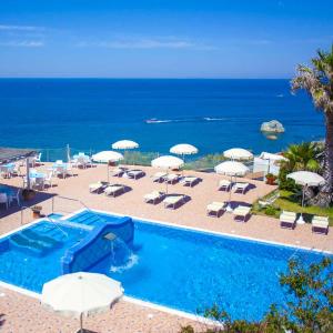 a swimming pool with umbrellas and chairs and the ocean at Hotel Albatros in Ischia