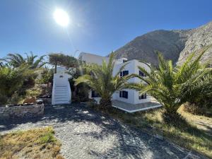 a white house with palm trees in front of a mountain at HONES - RELAX HOUSE in Perissa