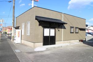 a building with a black door on a street at ゲストハウスHINATA in Hyuga