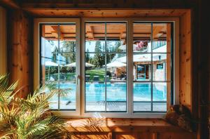 ventana con vistas a una piscina con sombrillas en Hotel Lindenhof, en Ramsau am Dachstein