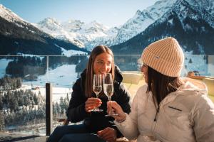 two women holding glasses of wine in front of a mountain at Gästehaus Mathies in Mittelberg