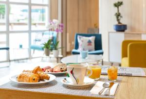 a table with two plates of breakfast foods and orange juice at BRIT Hotel Rouen Nord - Barentin in Barentin