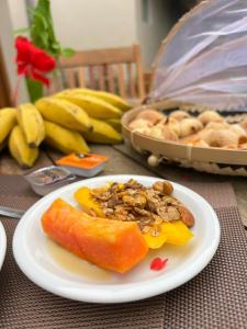 a white plate with a papaya on a table with bananas at Pousada Maresia in Fernando de Noronha