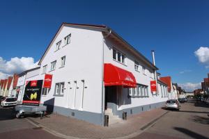 a white building with a red awning on a street at Mille Stelle Hotel in Eggenstein-Leopoldshafen