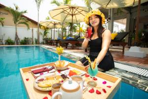 Eine Frau, die an einem Tisch mit einem Drink neben einem Pool sitzt. in der Unterkunft Cambana La Rivière Hotel in Battambang