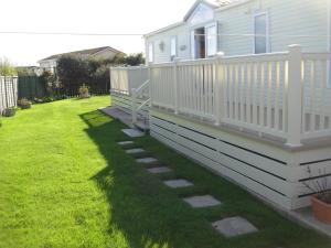 a house with a white deck and a yard at Bri-ann's Seaside Holiday Home NO VANS OR LARGE VEHICLES in Selsey