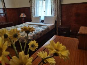 a bedroom with a bed and a table with yellow flowers at The Trevene Hotel in Nuwara Eliya