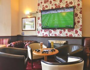 a bar with a tv on a wall with leather chairs at Bailey Ground Hotel in Seascale