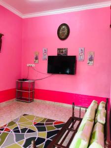 um quarto com uma parede rosa com uma televisão e um sofá em Homestay TokAbah em Pasir Puteh